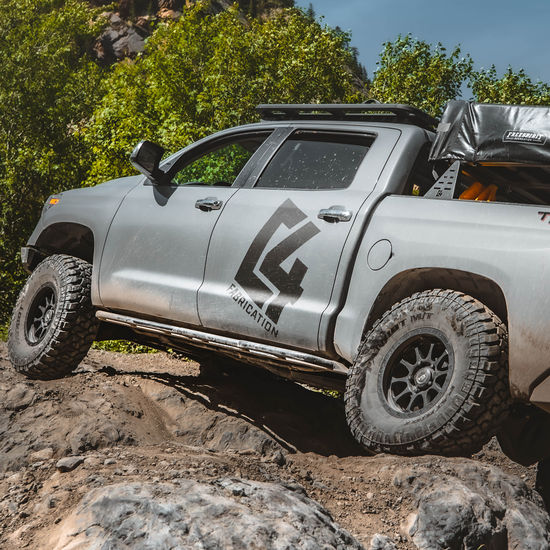 Modified Toyota Tundra CrewMax with C4 Fabrication sliders installed navigating a rocky trail.