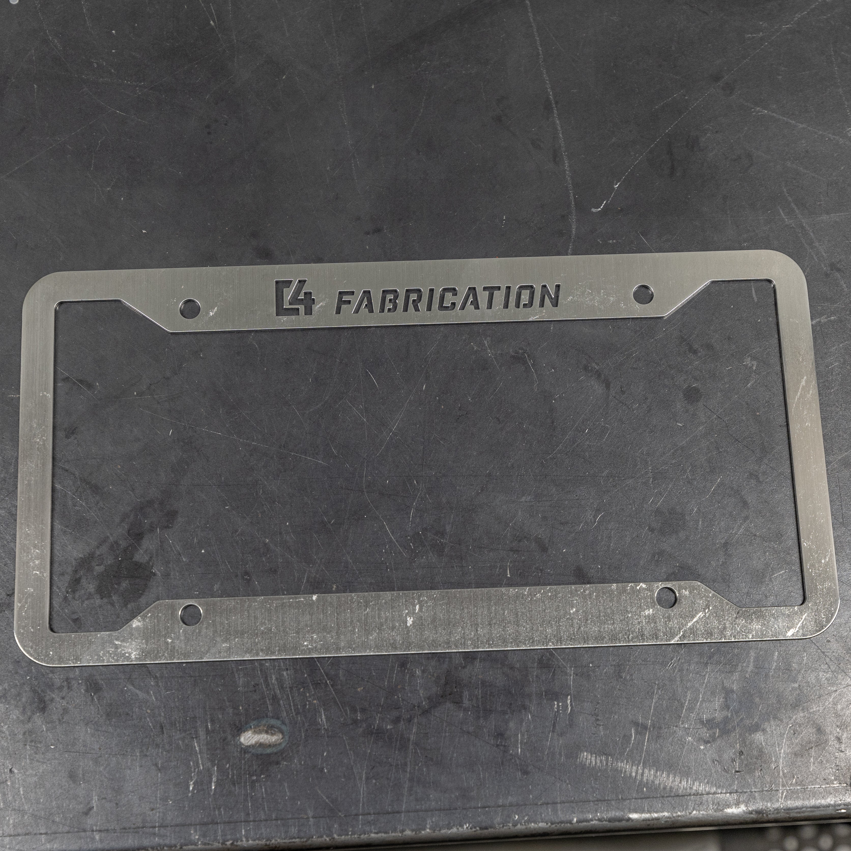 C4 License Plate Frame layed flat on a steel table to show the surface finish ready to be scuffed, polished or painted. 